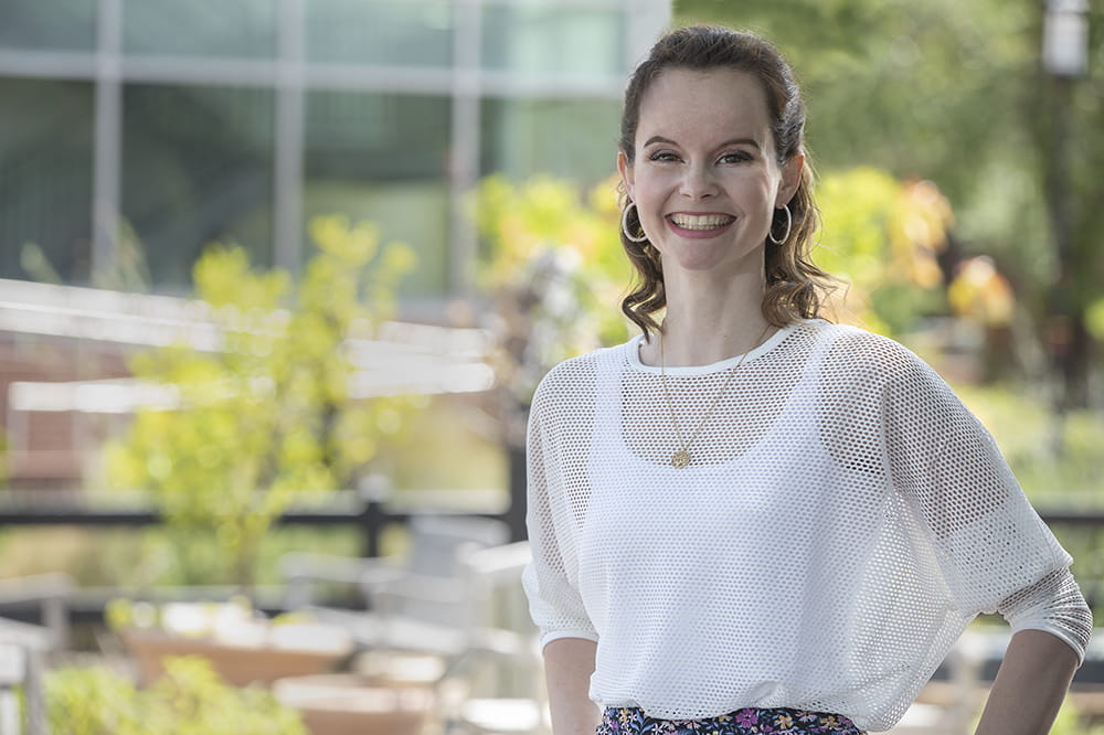 Crystal Wood, wearing a white blouse, stands outside, smiling.