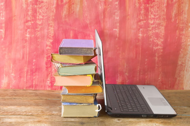 An image of a laptop with books stacked behind it.